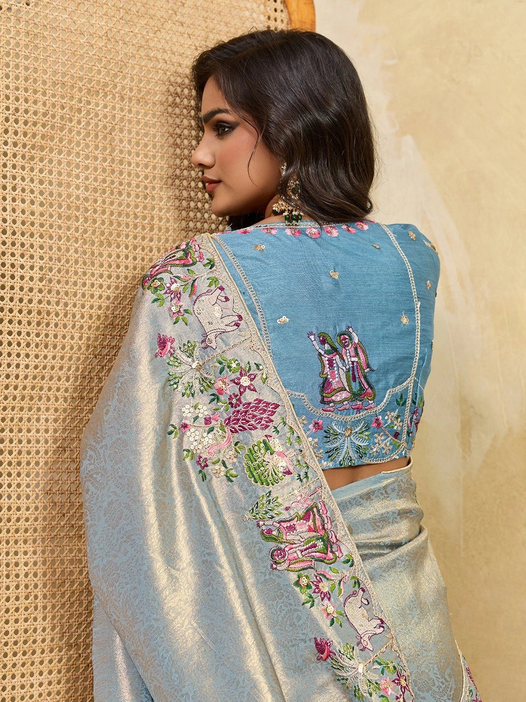 Woman wearing a traditional embroidered saree against a beige background